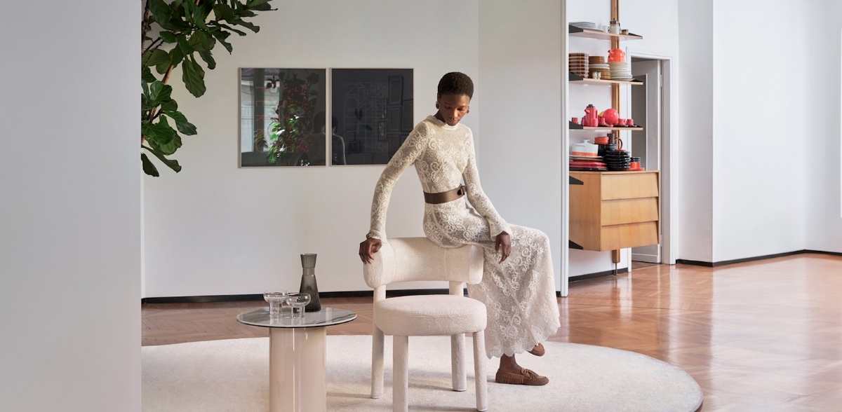 Εκρού δαντελωτή καρέκλα Calligaris Glen Soft Twinset σε φωτεινό λευκό σαλόνι, με γυναίκα να ακουμπά πάνω της, στρογγυλό γυάλινο τραπεζάκι, στρογγυλό χαλί και ξύλινο πάτωμα