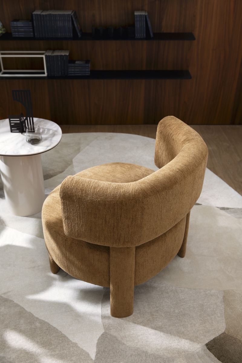 Καμηλό πολυθρόνα Calligaris Glen Soft σε σαλόνι, δίπλα σε στρογγυλό λευκό μαρμάρινο τραπεζάκι, με ξύλινη βιβλιοθήκη στο φόντο, πάνω σε χαλί με σχέδια