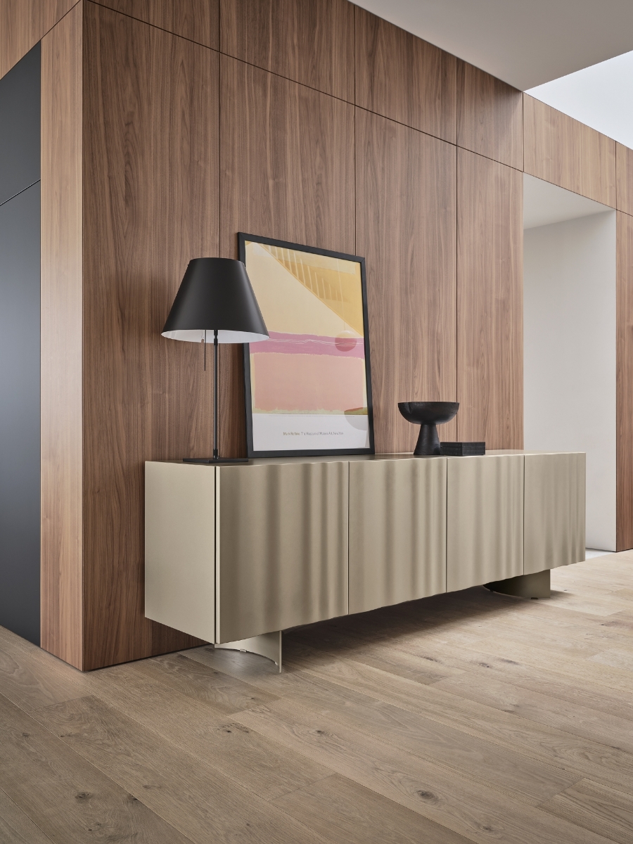 Μπουφές Calligaris Velo σε σαμπανί απόχρωση με ανάγλυφες πόρτες σχεδίου πέπλου και μεταλλική βάση, σε τοίχο με ξύλο καρυδιάς με μαύρο φωτιστικό και αφίσα — Adamopoulos Casa Ideale, επίσημος αντιπρόσωπος Calligaris στην Ελλάδα