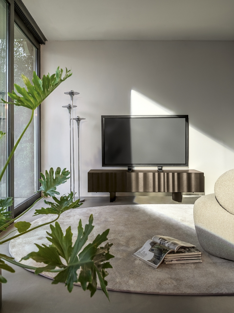 Έπιπλο τηλεόρασης Calligaris Velo σε καφέ μόκα απόχρωση με ανάγλυφες πόρτες-πέπλο, σε σαλόνι με τηλεόραση, λευκό μπουκλέ καναπέ και πράσινα φυτά — Adamopoulos Casa Ideale, επίσημος αντιπρόσωπος Calligaris στην Ελλάδα